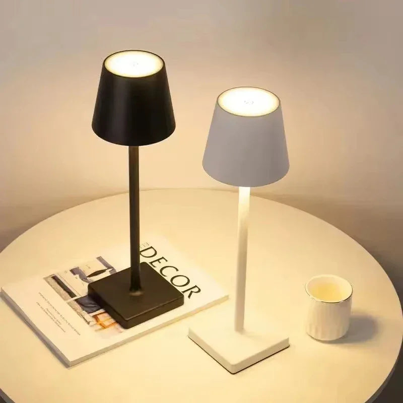 Two table lamps, one black and one white, on a round surface with a magazine and a cup.